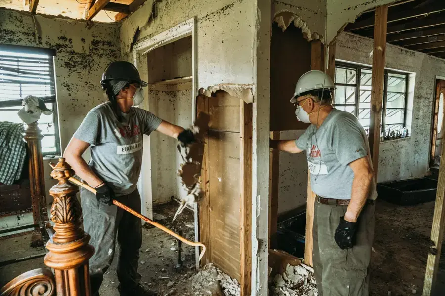 Workers in masks tearing out soaked drywall after flood water in the Lancaster area
