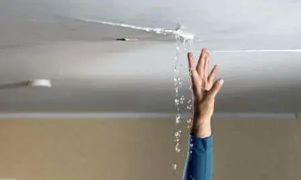 Water streaming through a cracked ceiling onto a raised hand during a ceiling leak in Lancaster, SC