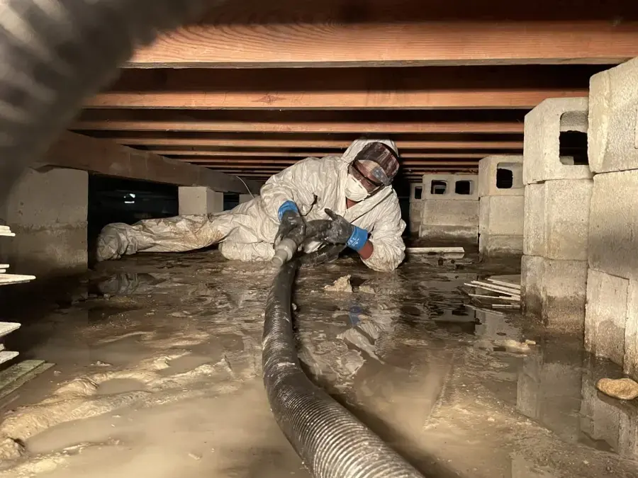 Technician in a protective suit running an extraction hose through a flooded crawl space in Lancaster, SC