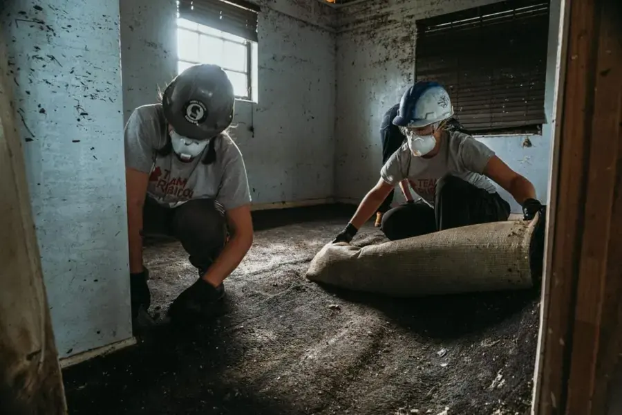 Workers in masks rolling up mud-soaked carpet after storm flooding in a Lancaster area home