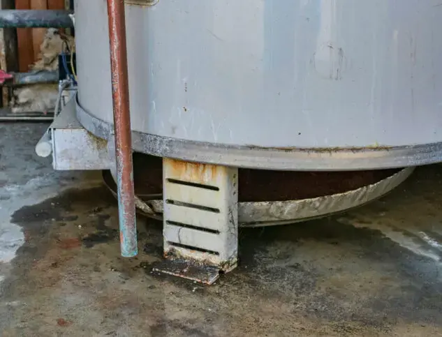 Leaking water heater with rust and standing water around its base in a Lancaster, SC home